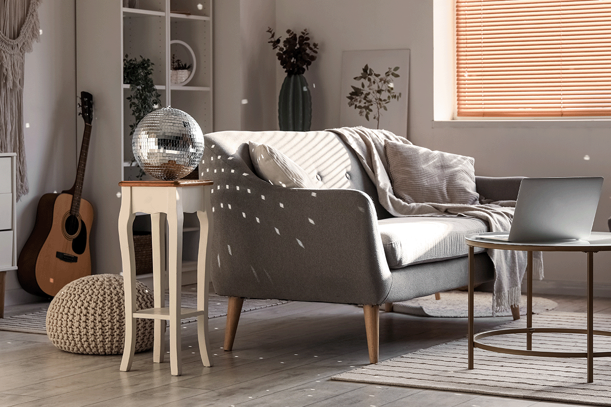 a gray living room with a gray sofa. Behind the sofa there is an end table that has a disco ball, and its reflection is lighting up the entire room. 