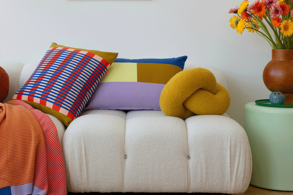 there is a white couch under colorful pillows. the pillows are pruple, yellow, blue, and with patterns of red.