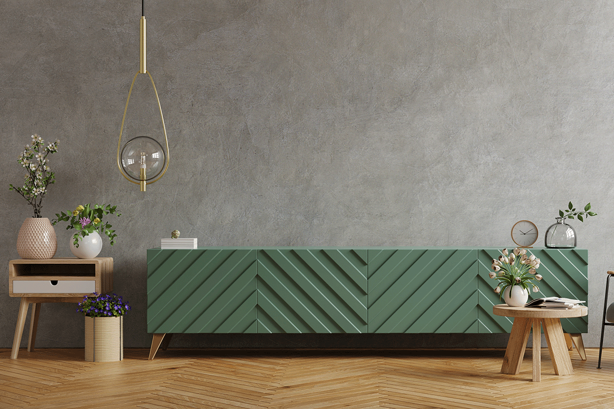Green Console Table with concrete wall behind and wooden floor underneath. There are light colored end tables at either side with multiple flower pots and flowers in them. There is a gold light fixture at the left of the room. 