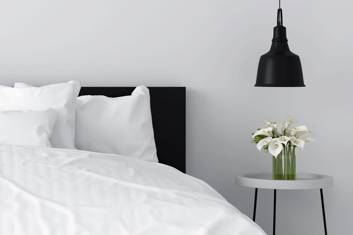 A white bedroom with black headboard, a small night stand, and a black light fixture overhead