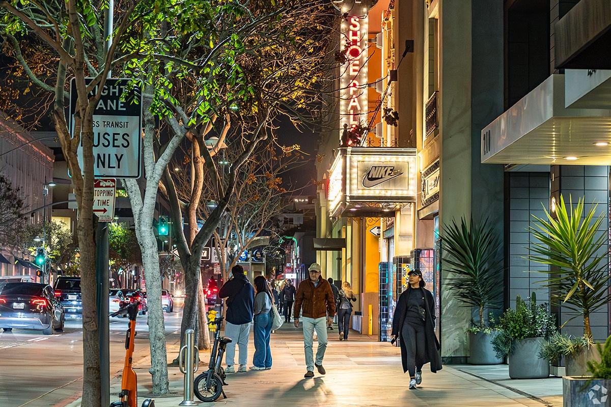 People walk late at night in Los Angeles on brightly lit and busy streets.