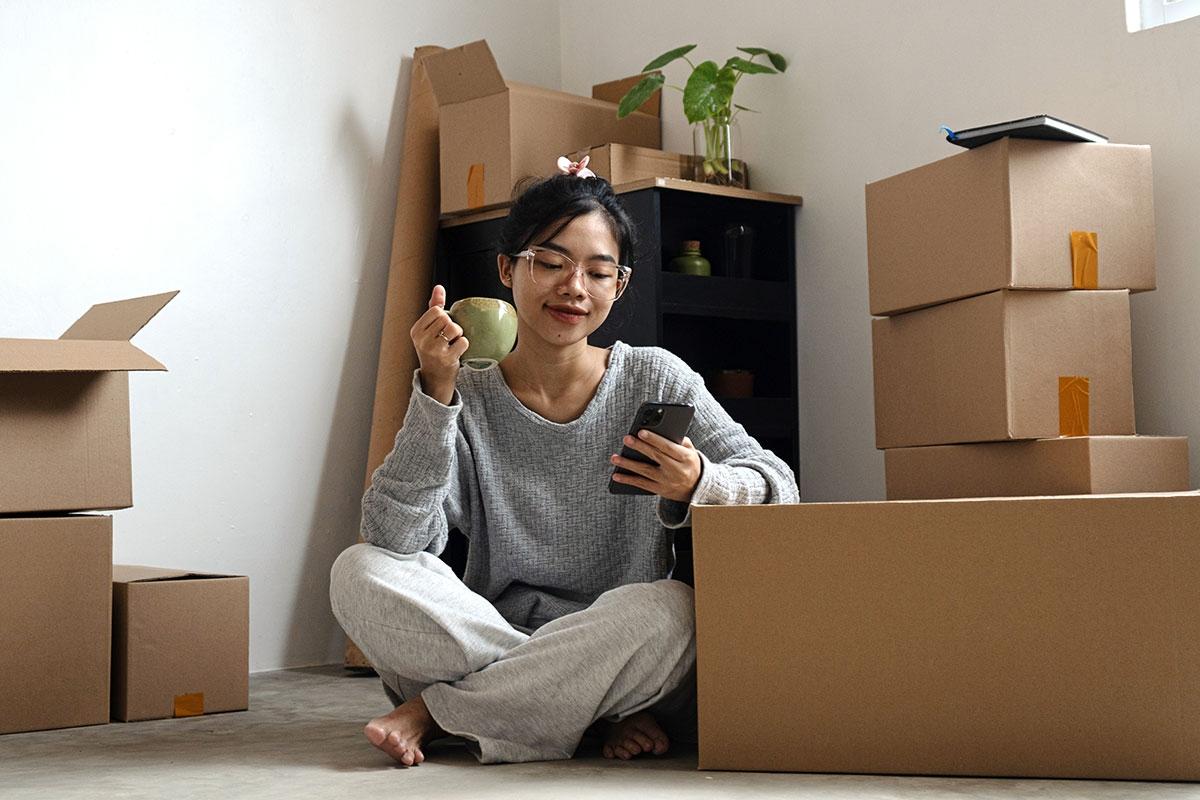 Gen Z renter looking at phone while unpacking in new apartment. 