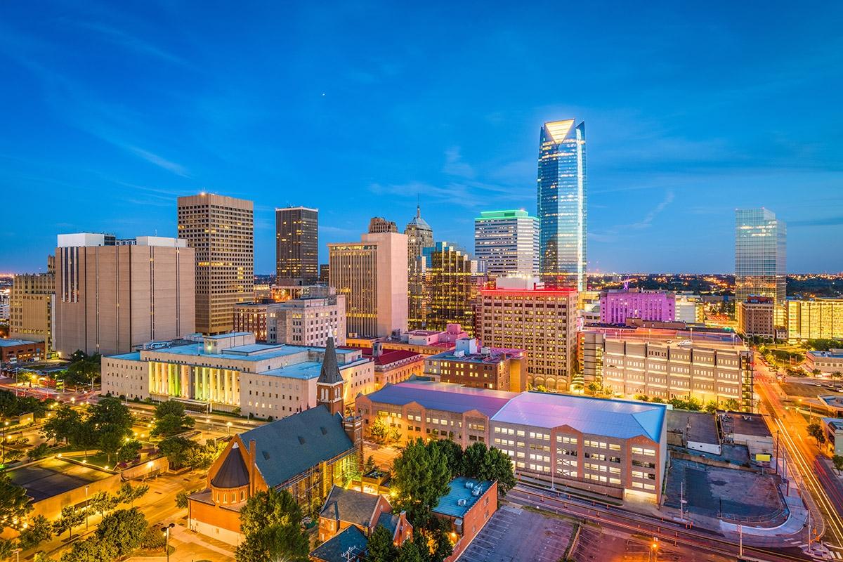 Tall buildings in Downtown Oklahoma City rise next to historic churches during the evening.