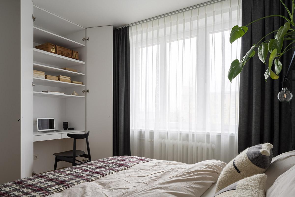 A desk sits in a wardrobe in a bedroom with a bed behind it.