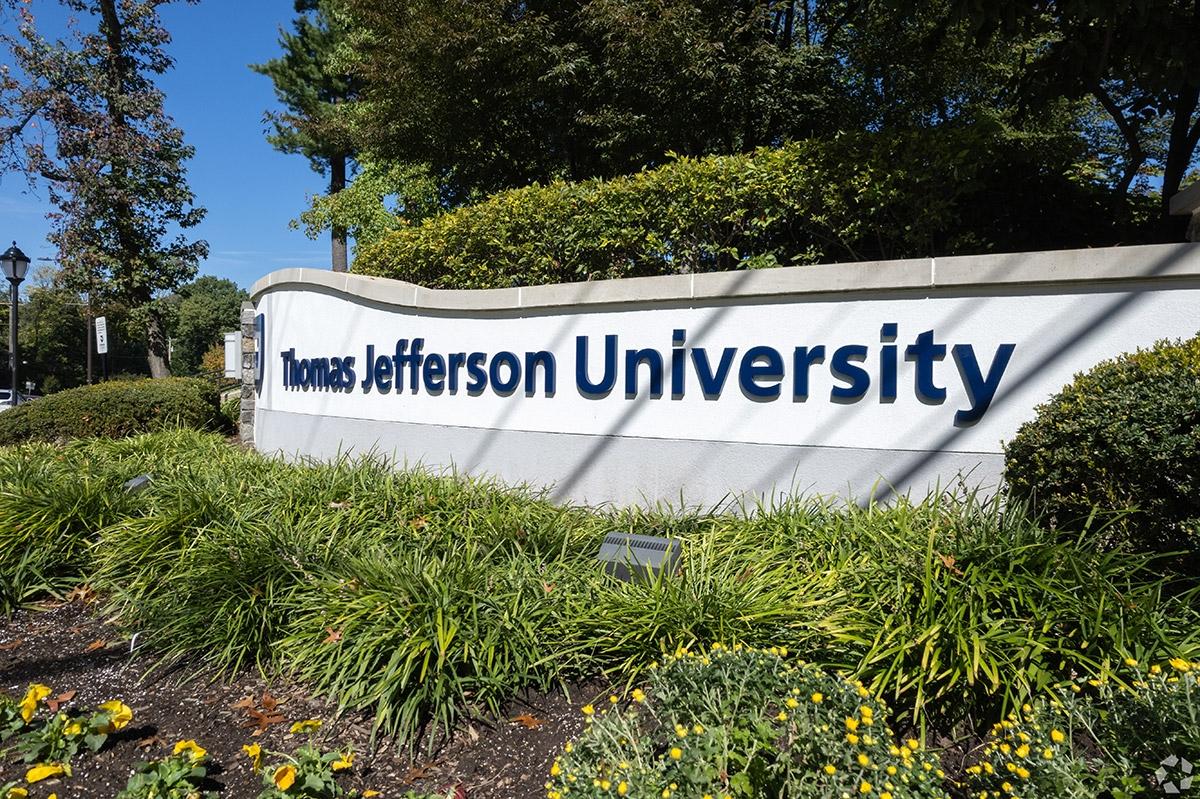 A sign showing off the name of Thomas Jefferson University behind landscaped plants.