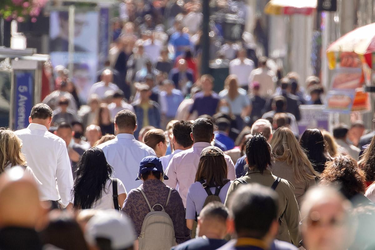 A ton of people walking down the busy sidewalks in a city.