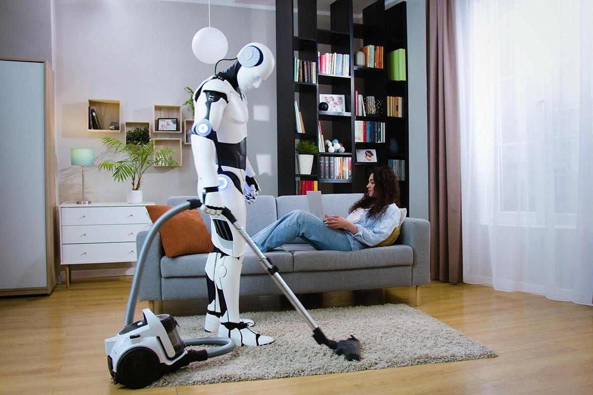 A woman sitting on a couch, relaxing, as a robot vacuums her apartment.