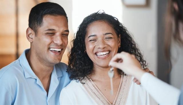 A smiling couple is handed a key to their new apartment.