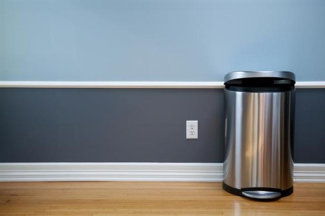 A stainless steel trash can against a two-tone blue wall.
