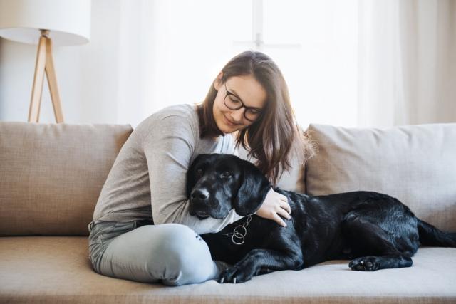 Woman hugging her dog as they sit on a couch.