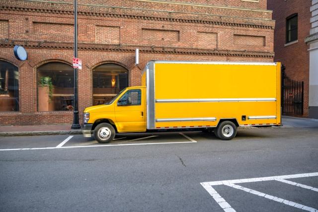 A yellow box truck is parked outside a brick building in Boston.