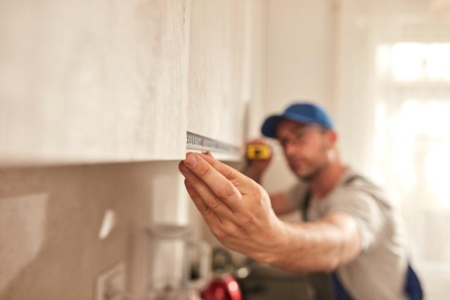 Contractor measures kitchen cabinets for apartment renovation. 