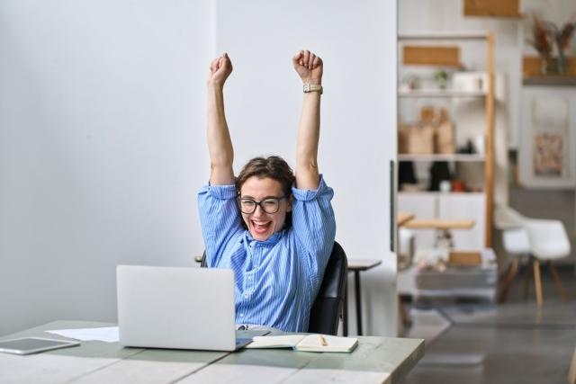 Lady sitting at computer with arms raised in excitement