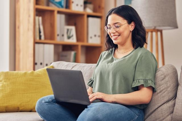 Young lady sitting on couch in apartment while typing on laptop.