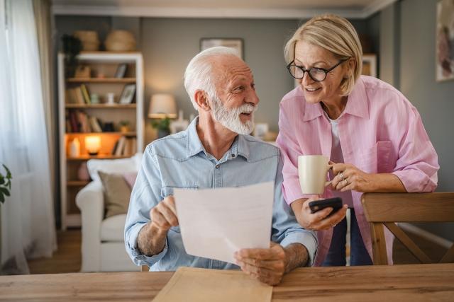 Senior couple looking at mail with excitement in apartment.