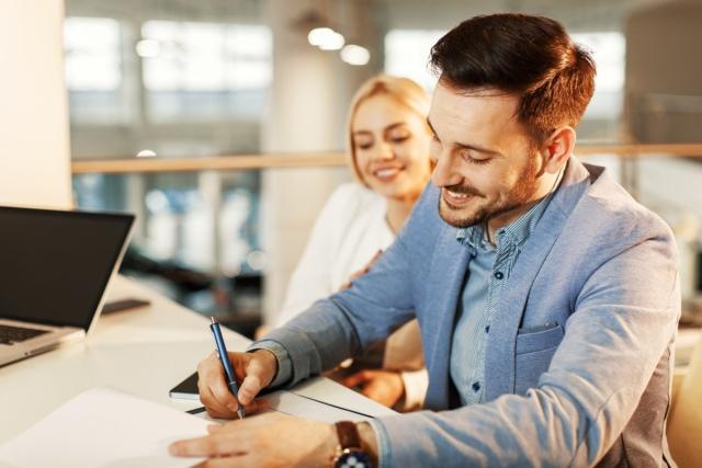 A couple sitting at a desk filling out papers in a business office.