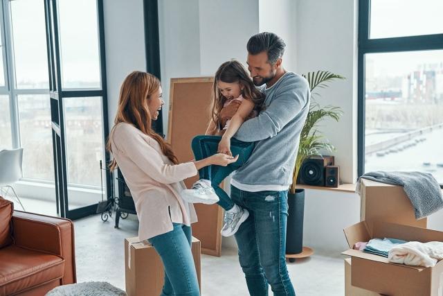Man holding kid up with woman holding the kid's hands as they all laugh in new apartment.