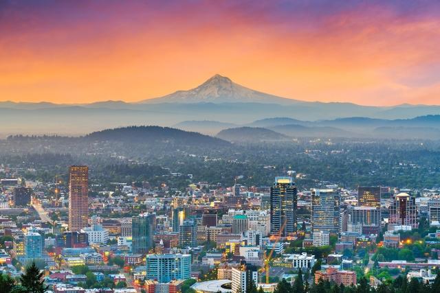 Oregon mountains rise behind major cities during the sunset.