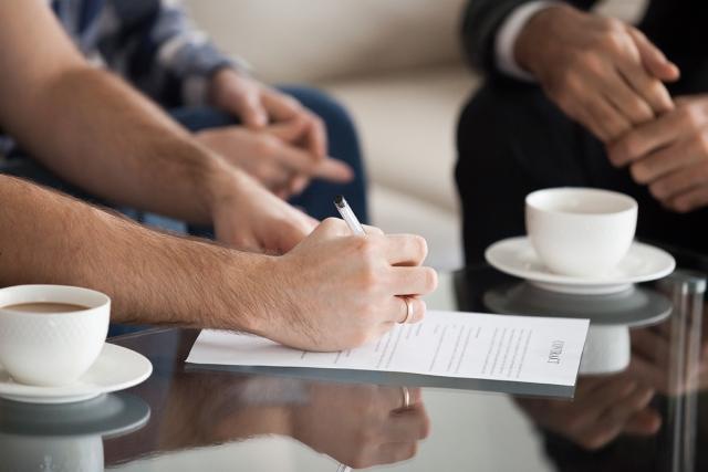 A person signs a lease agreement next to two other people.