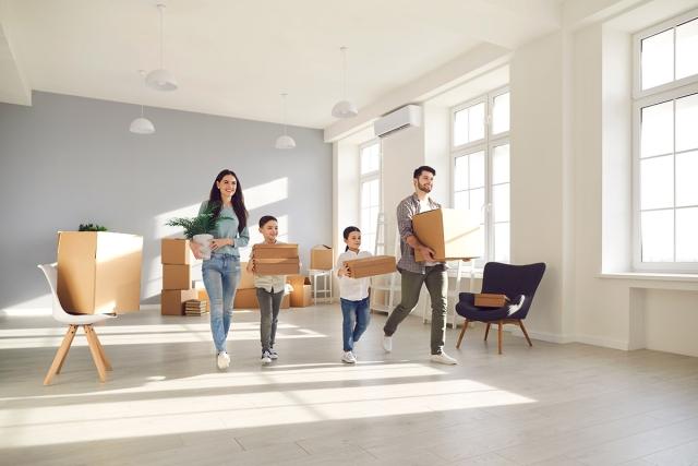 A family carrying moving boxes and walking in an empty apartment.