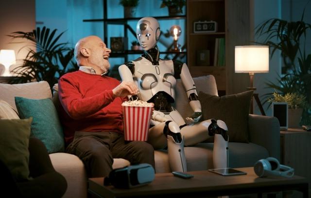 Guy sitting on a couch, eating popcorn, and laughing next to a robot.
