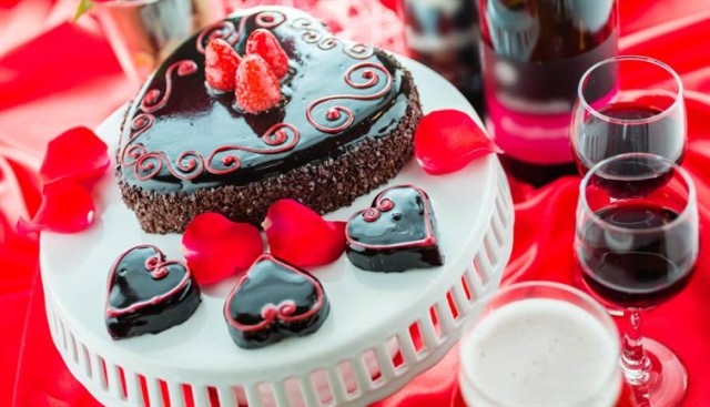Heart-shaped chocolate cakes adorned with raspberries sit next to glasses of wine.