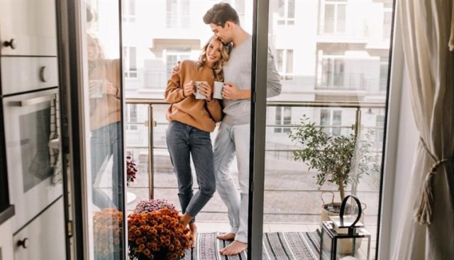 A couple standing on their apartment balcony with coffee mugs.