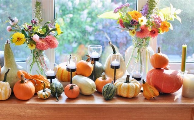 Display of flowers, candles, and pumpkins in front of a window.