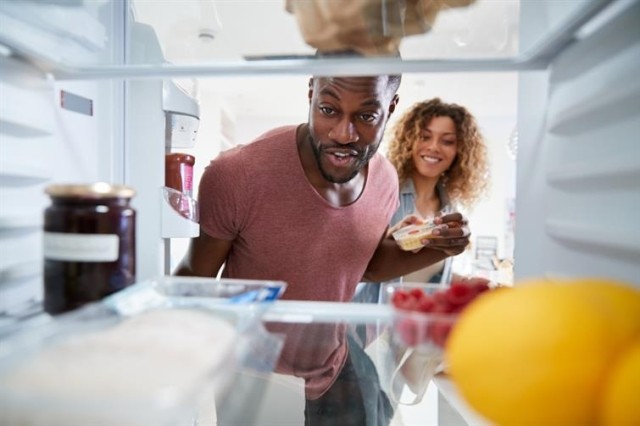 Two people stare into a refrigerator. 