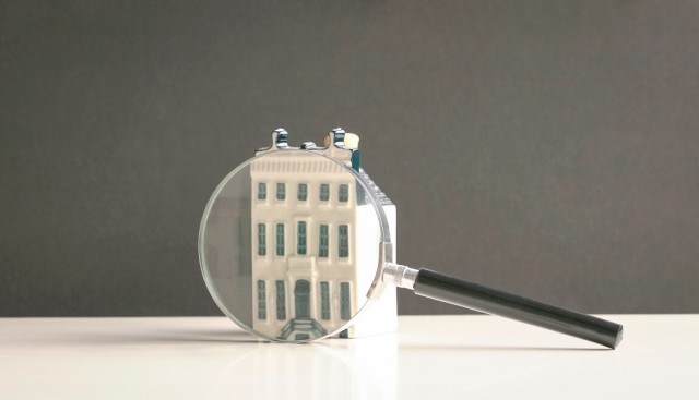 A magnifying glass sits in front of a small replica of an apartment building.