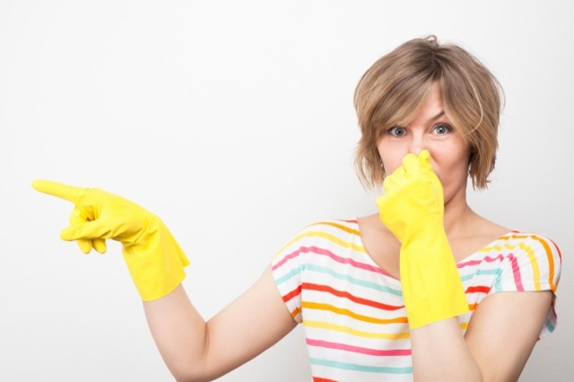 Woman wearing cleaning gloves and holding her nose.