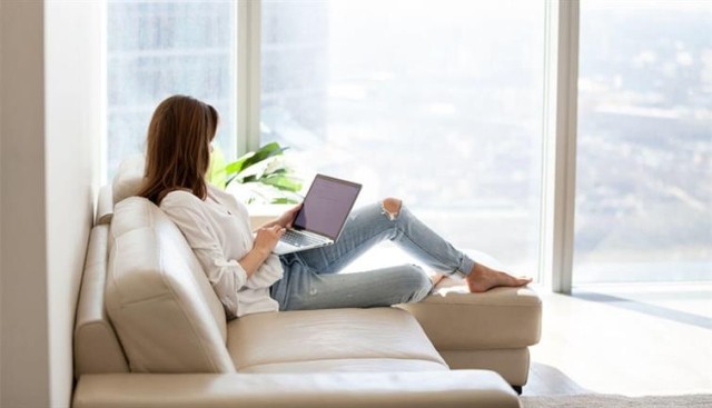 Woman sitting on a couch searching on a laptop computer. 