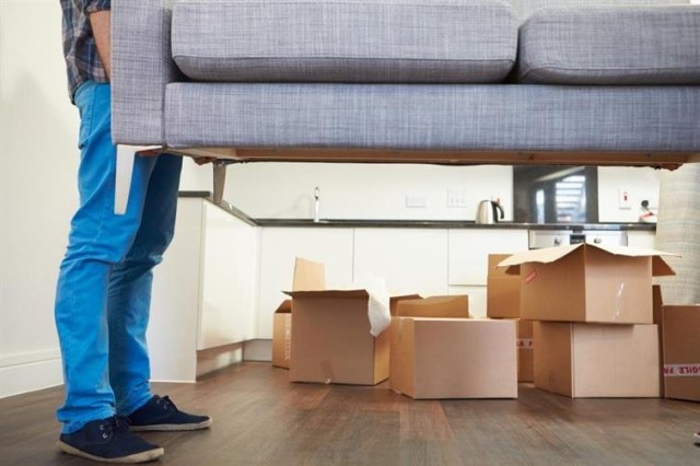 A figure lifting a couch over packed boxes