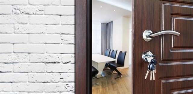 A door with keys in the lock stands ajar revealing a room with a table and chairs.