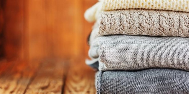 A stack of sweaters sitting on a wooden bench.