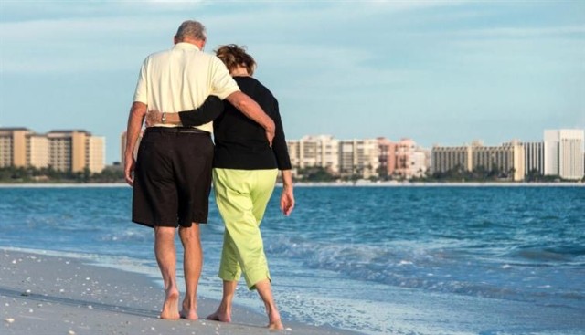 A couple walking on the beach with their arms around each other.