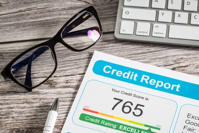 A pair of glasses sits next to a copy of a credit report showing a 765 credit score.