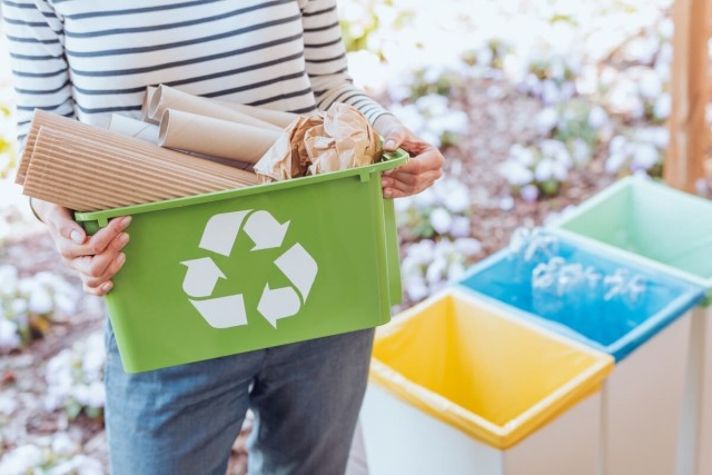 A woman carries a bucket of recycled items.