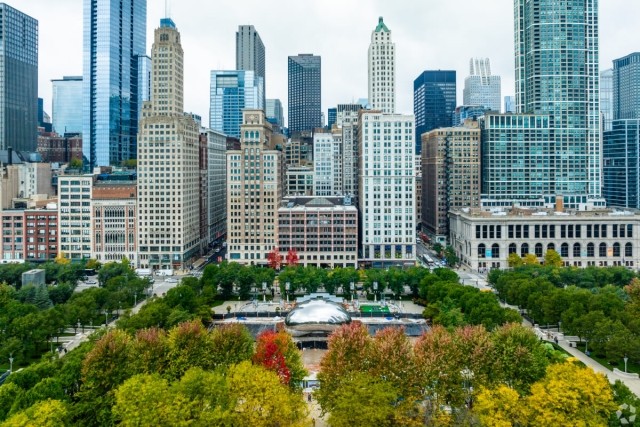 An aerial view of Millennium Park in Chicago shows The Bean sculpture in front of the Chicago skyline.