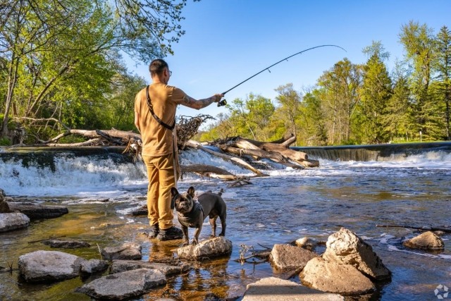 Man fishing with his dog near a waterfall at Kletzsch Park in Glendale, Wisconsin, ideal for pet-friendly apartment residents who enjoy nature and outdoor recreation. 