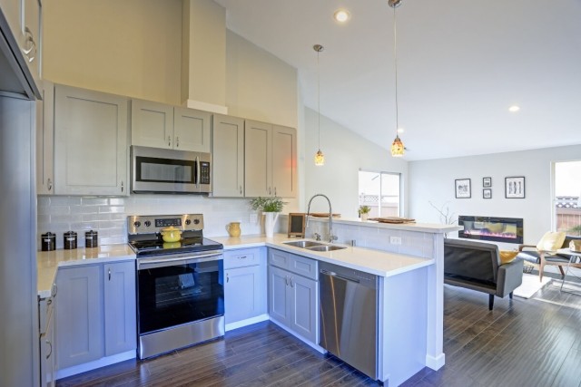 A view of an apartment with vaulted ceilings, pendant lights, wood floors, and stainless steel appliances.