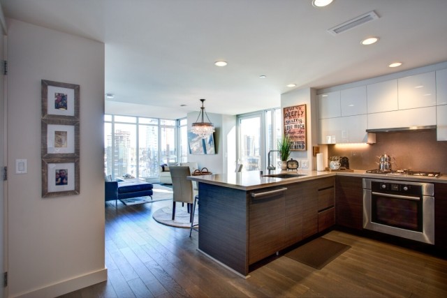 A view of a luxury apartment with stainless steel appliances, hardwood floors, and a chandelier.