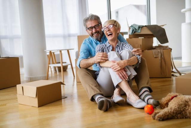 Senior couple sitting on floor, laughing and embracing as they move into their new apartment with their dog.