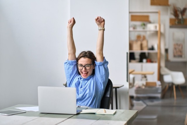 Lady sitting at computer with arms raised in excitement