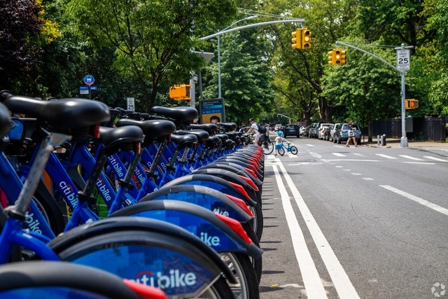 Citi bikes are lined up and charging on a New York street lined with trees.