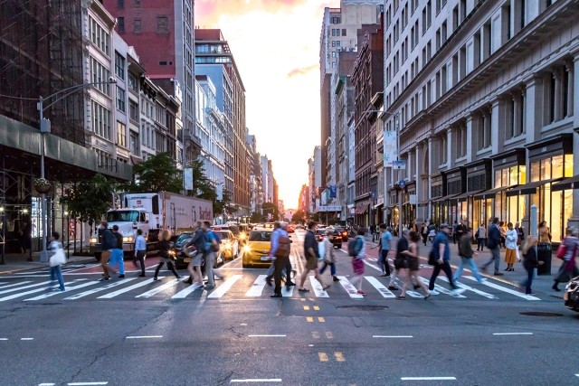 People walk across a crosswalk in a busy city.