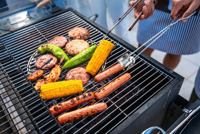 A photo of people grilling burgers, hot dogs, and veggies. 
