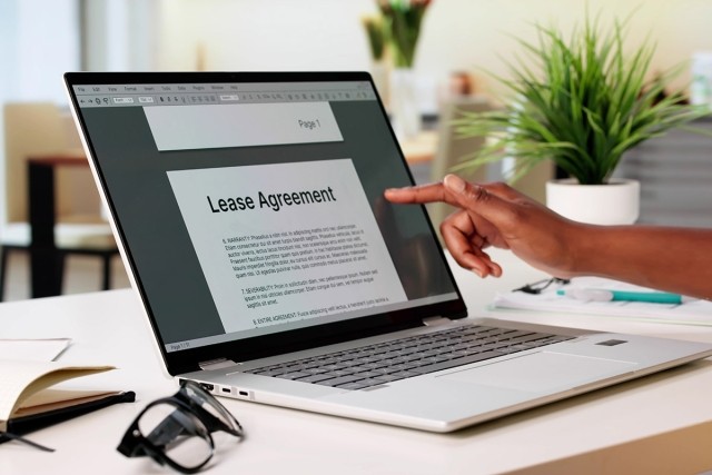 A hand pointing at a computer with an online lease agreement on the screen.