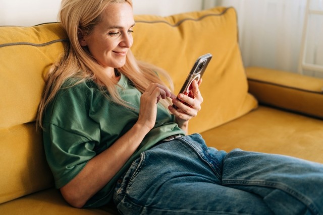 A woman sitting on the couch scrolling on her phone.