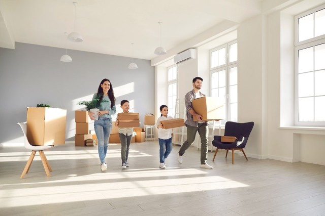 A family carrying moving boxes and walking in an empty apartment.